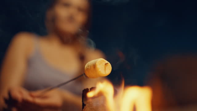 SLO MO Close-Up Hand of Woman Roasting Marshmallow Over Bonfire While Camping at Night