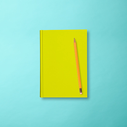 Overhead shot of a closed yellow book with a pencil on light blue background, with clipping path.\nBack To School concept.