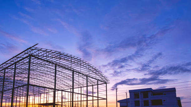 istock Silhouette metal warehouse structure with office building in construction site area against sunset sky background 1588985664