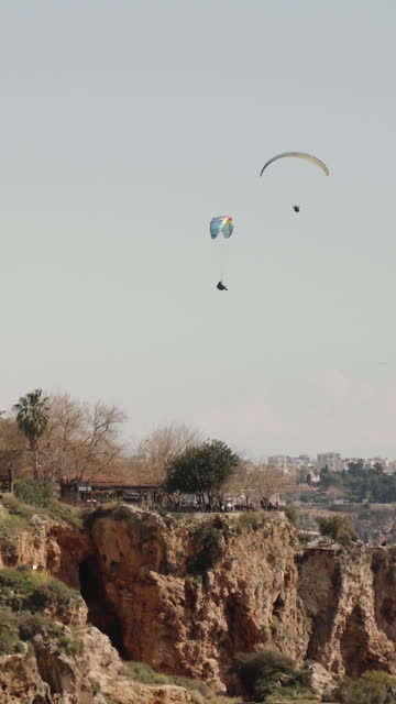 People on a paraglider fly over a cliff in the sea. Flag of Turkey. Vertical video.