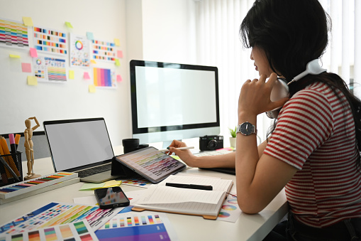 Young creative woman working with color palette, choosing color samples for design project at graphic studio..