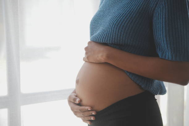 szczęśliwa kobieta w ciąży dotykająca brzucha przed białą ścianą - ciąża zdjęcia i obrazy z banku zdjęć