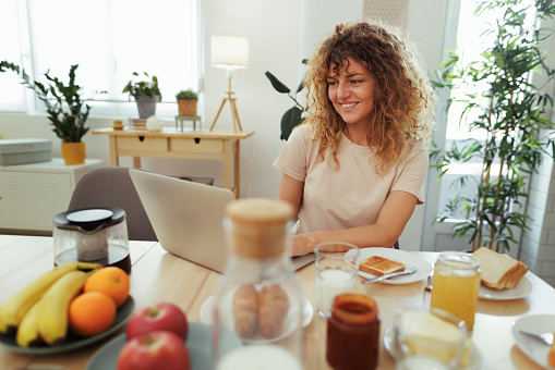 Young smiling woman working while having breakfast at home