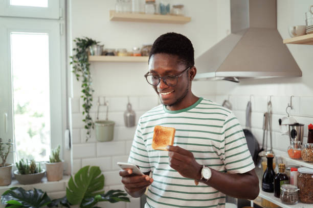 istock Young casually clothed man text messaging in a domestic kitchen 1589243146