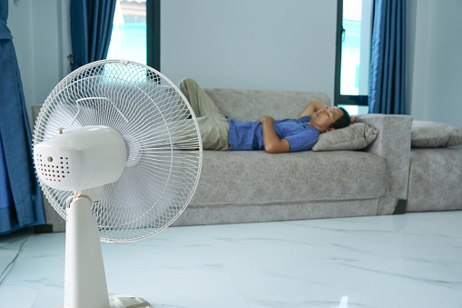 asian men turn on the fan while sleeping in the living room. simple energy in the home.