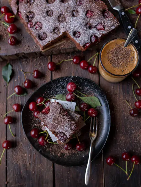Rustic food background with homemade baked chocolate cake with cherries. Served with dalgona coffe on dark wooden background from above.