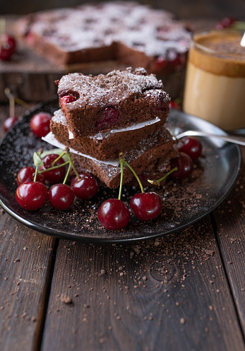 Delicious homemade cherry chocolate cake for christmas season. Served with a glass of dalgona coffee on rustic and wooden table background. Closeup, front view with copy space.