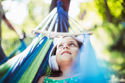 Little girl lying down in hammock alone and listening to music with headphones at backyard