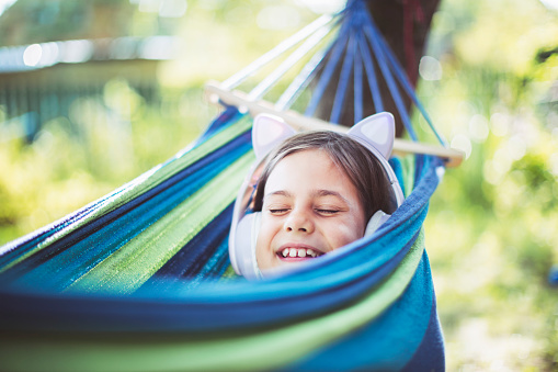 Little girl lying down in hammock alone and listening to music with headphones at backyard