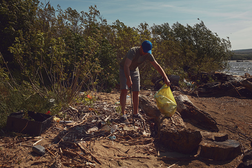 Volunteer and environmental activist cleaning dirty river shore filled with trash.