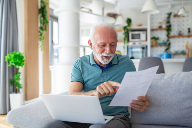 istock Surprised laughing happy old mature retired man looking through paper document, feeling excited analyzing financial information, getting taxes refund or bank loan approval at home. 1589336373