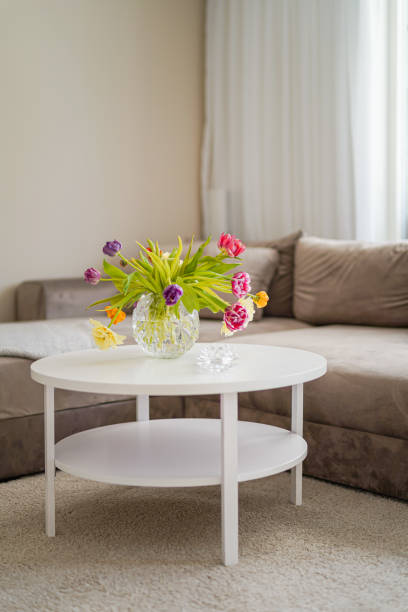 istock Interior design warm beige sofa and white round table with colourful flowers on the white carpet 1589338595
