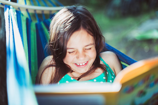 Little girl lying down in hammock and laughing at funny story from the book