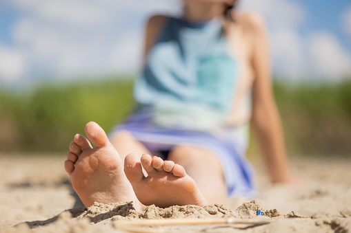 Beach feet closeup - barefoot woman walking in ocean water waves. Female young adult legs and toes wearing an ankle bracelet anklet relaxing in summer vacation travel.