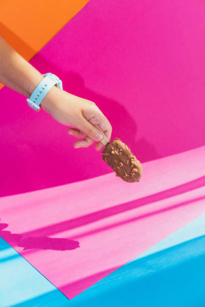 カラフルな背景にスティックにチョコレートアイスクリームを手で持つ - lolly pop ストックフォトと画像