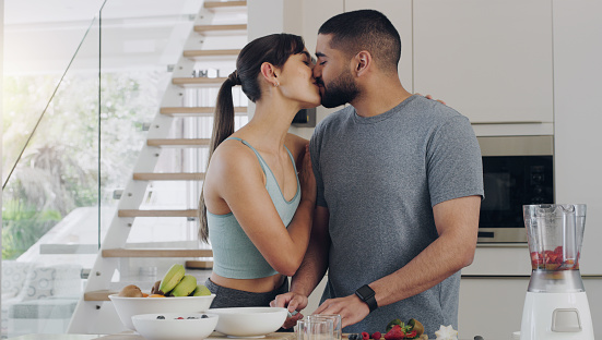 Love, cooking and couple kissing in kitchen while preparing a healthy, fresh and diet breakfast. Happy, bonding and young man and woman with intimate moment while cutting fruit for smoothies together