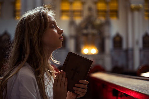 Little girl with Bible praying in Catholic church