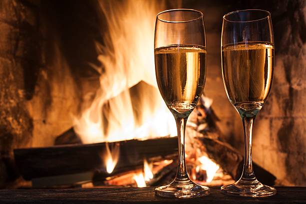Two champagne glasses on table by a romantic fireplace stock photo