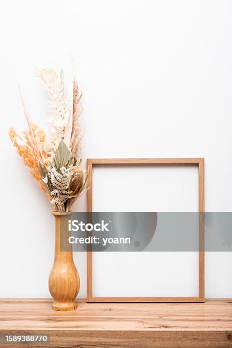 istock Decor wooden picture frames against wall with decor flowers on wooden chest of drawers. 1589388770