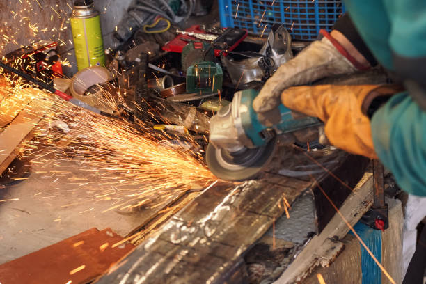 Man working with rotary angle grinder at workshop, closeup detail, orange sparks flying around stock photo