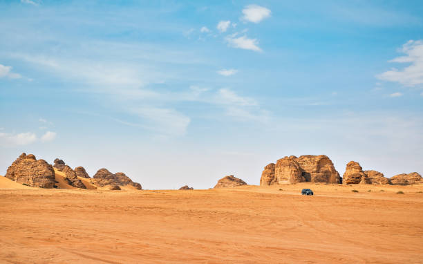 Typical desert landscape in Alula, Saudi Arabia, sand with some mountains, small offroad vehicle, local man and camels at distance stock photo