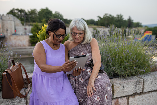 Two senior women using a digital tablet in a city while taking a break from walking