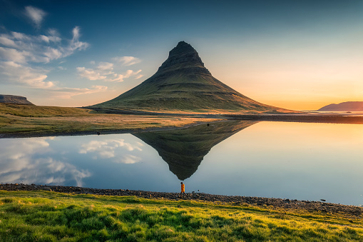 Aerial view of majestic symmetry volcano Kirkjufell mountain with lake reflection and male tourist standing during sunrise morning in summer at Snaefellsnes peninsula, Iceland