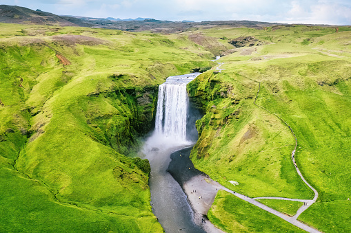 Aerial view of majestic Skogafoss waterfall flowing from cliff surrounded by lush landscape in summer at Iceland. Famous tourist attractions and landmark destination