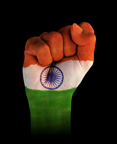Vertical cutout of a fist of hand painted in three vibrant colored bands in orange, white and green with blue wheel with spokes or Ashok Chakra in the middle over black background. The image denotes confidence, strength and determination.There is no text and Copy space for text. Can be used for national festivals, events, national teams related backdrops like Indian Republic Day, Independence Day celebrations.