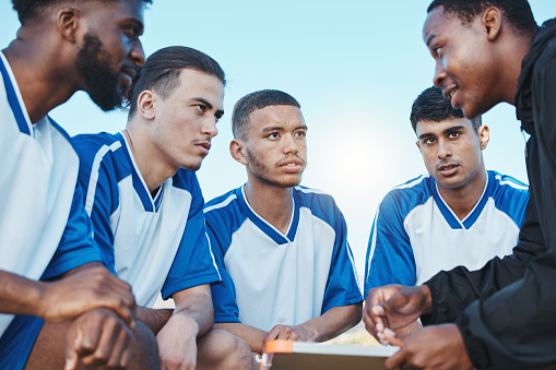 Sports, soccer coach and a team talking on a field for fitness exercise or outdoor game. Football formation, club and diversity athlete men listen to plan for coaching, scrum and training strategy