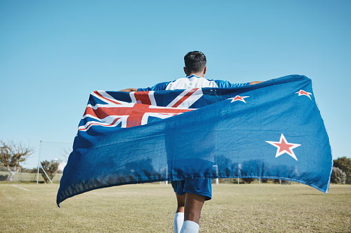 Flag, sports and a man running on a field with a blue sky to celebrate outdoor. Banner, champion and athlete person with patriotism and pride after winning competition to support New Zealand country