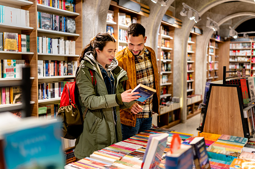 A young man and woman are browsing the shelves of a quaint book shop, eagerly searching for their next literary adventure