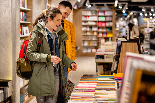 A young man and woman are enjoying each other's company as they playfully pick out books to read together in a cozy bookstore