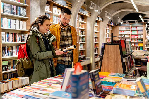 A young couple is spending quality time together in a book store, carefully selecting books that they can read and discuss as a couple