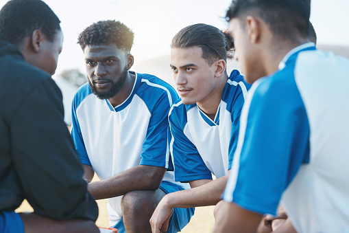 Sports, huddle and soccer team talking to their coach before a match, training or tournament. Fitness, teamwork and male football player or athletes planning a game strategy at practice on a field.