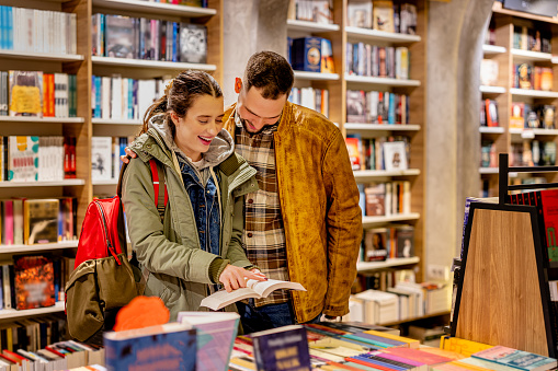 A young man and woman are checking out the latest literary offerings at a trendy book store, excited to discover their next favorite book