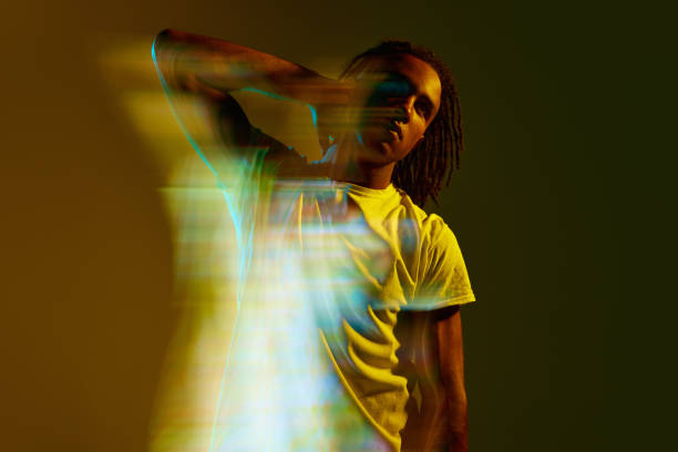 istock Stylish young african man posing over gradient green background in neon light. Mixed light effect. Hologram 1589449106