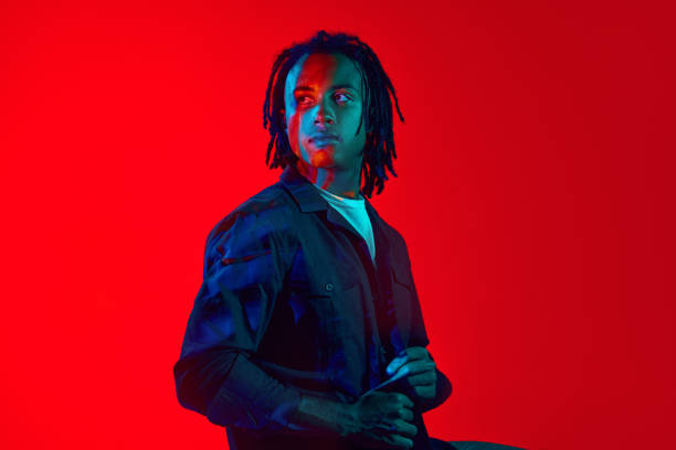 istock Handsome young african guy with colorful neon filter reflection on face posing against red background in neon light 1589449221