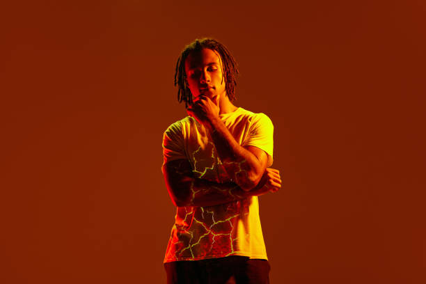 istock Handsome young african man with fire light reflection on body, hologram standing against brown background in neon light 1589449611