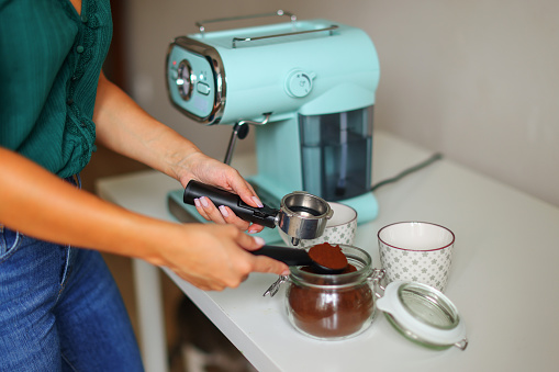 Close-up image of woman hand using blue coffee machine when making big mug of coffee at home