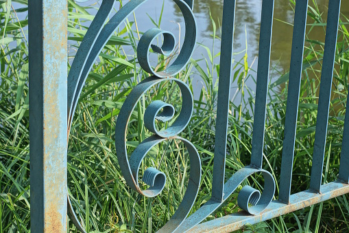 part of a railing design made of blue metal bars in a wrought iron pattern in green grass outdoors