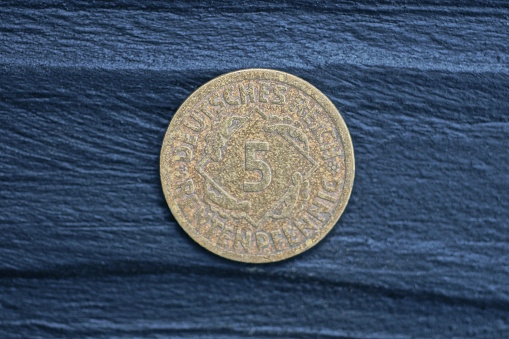 one old german brown five pfennig coin lies on a black wooden table