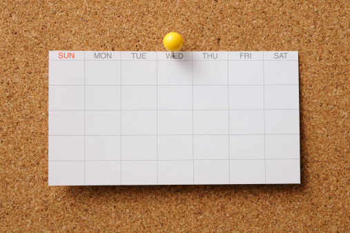 Close-up of blank calendar pinned on cork board with yellow thumbtack.