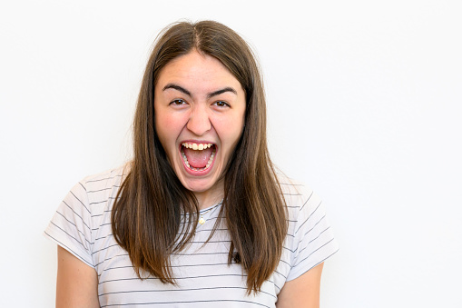 Front view of a young woman screaming at camera standing in front of a white wall