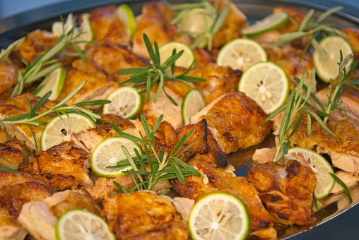 Pan full of pieces of roasted chicken. Decorated with slices of lime and rosemary.
