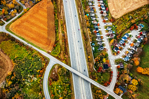 A tale of two: A drone view of a middle-class neighborhood on one side of the interstate and a rural farm ground on the other side of the road. The image is representing urban sprawl. The scene is in early Autumn.  Roads and rows of houses. The areal image is taken between Dayton and Cincinnati Ohio.