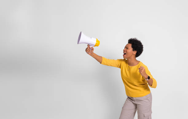 istock Young female activist holding megaphone and screaming while protesting over white background 1589524341