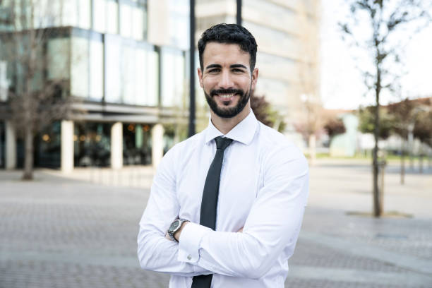 istock Confident executive standing at camera with arms folded. Handsome businessman smiling with an urban background. Financial concept. 1589546033