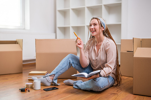 Modern ginger woman with braids writing in notebook while moving in new home.