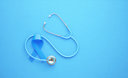 Prostate cancer awareness ribbon and stethoscope on blue background. Horizontal composition.